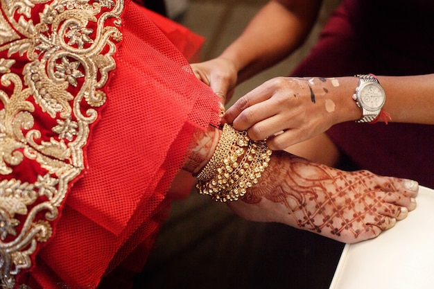 Woman puts golden bracelet with bells on bride's leg painted