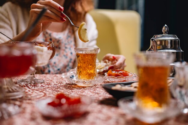 Woman puts lemon slice into tea in crystal armudu glass