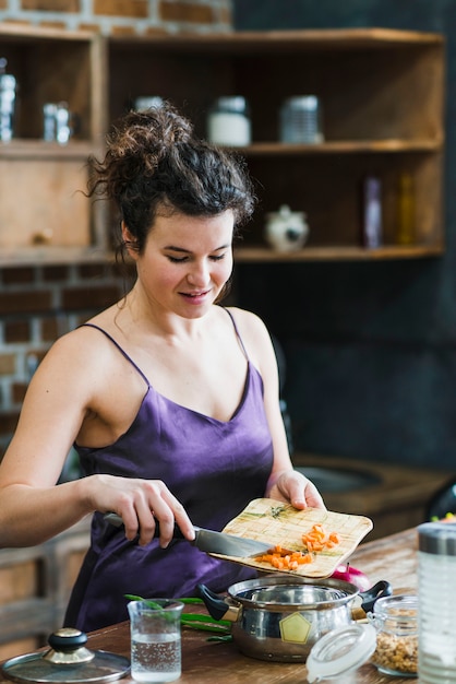 Woman putting cut carrot into saucepan