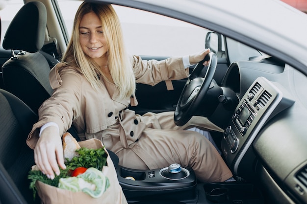Женщина кладет еду в сумку для покупок в ее машину