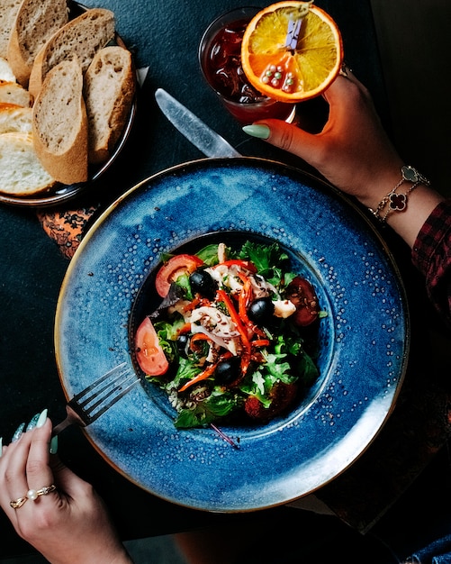 Woman putting a fork to eat mixed seasonal vegetable salad inside blue plate.