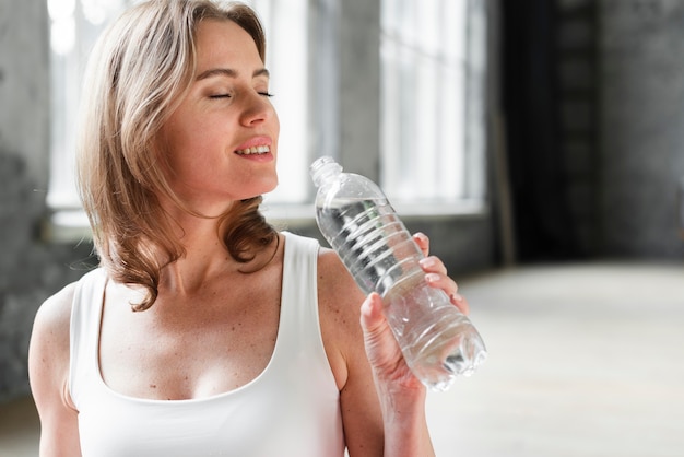 Женщина кладет бутылку воды в рот