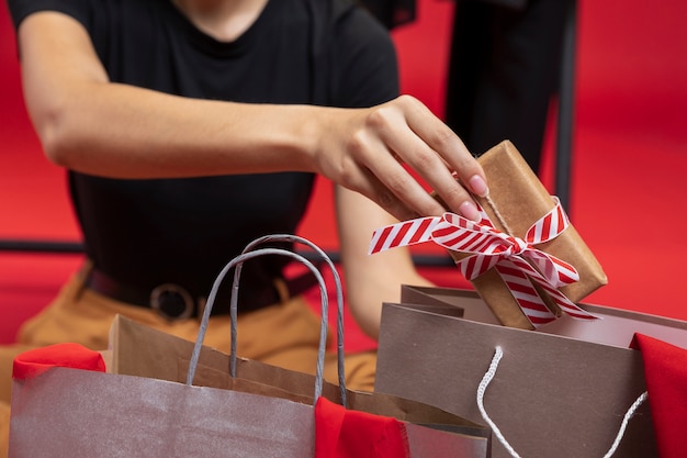 ラップされたギフトを買い物袋のクローズアップに入れて女性