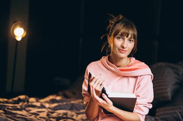 Woman in pygama sitting in bed and reading book