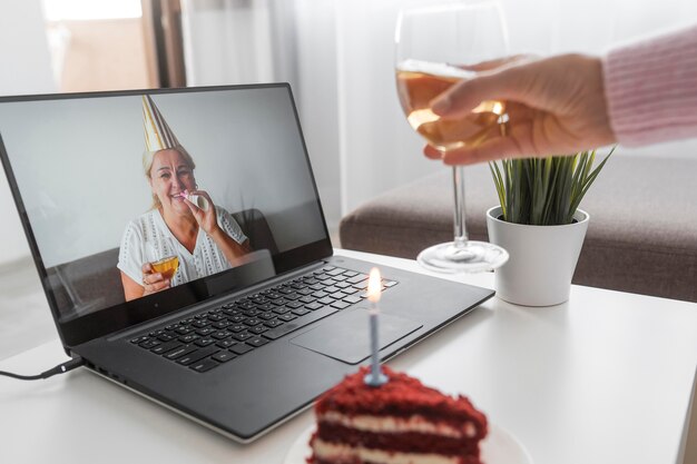 Woman in quarantine celebrating birthday with friends over laptop and cake