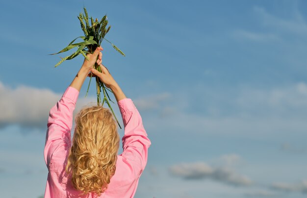 Woman raised her hands to the sky in the hands of ears of wheat. Blue sky with clouds, selective focus with copy space, idea for banner or background