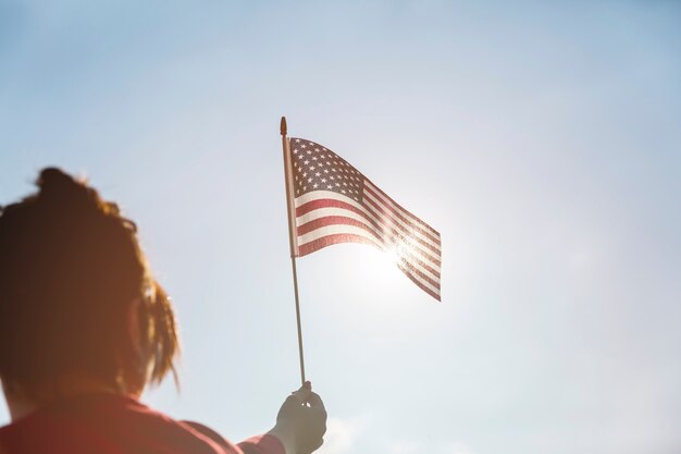 明るい太陽にアメリカの国旗を上げる女性