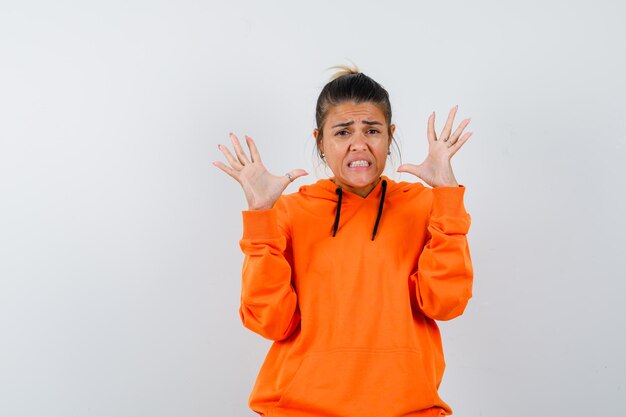 woman raising hands in aggressive manner in orange hoodie and looking disgusted