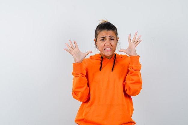 woman raising hands in aggressive manner in orange hoodie and looking disgusted