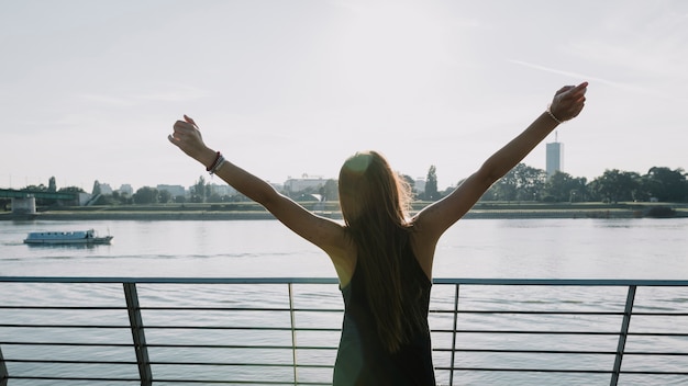 Woman raising her arms in front of river at outdoors