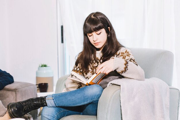 Woman reading book in armchair