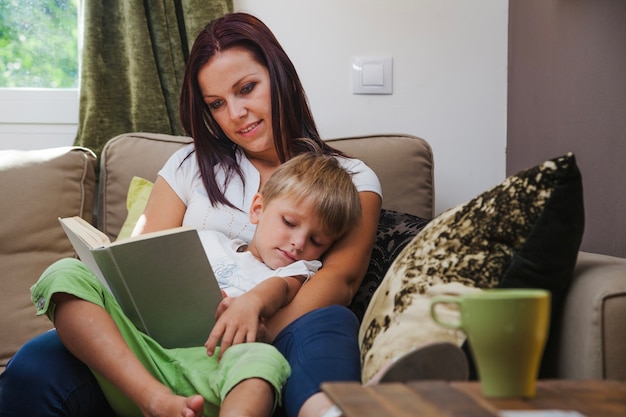 Woman reading book to boy sitting on sofa