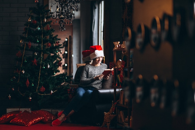 Woman reading book by christmas tree