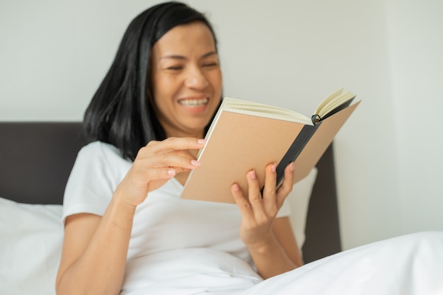 Женщина, читающая книгу дома в спальне.