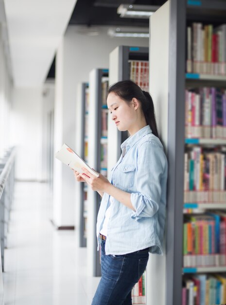 Woman reading a book leaning on a shelf