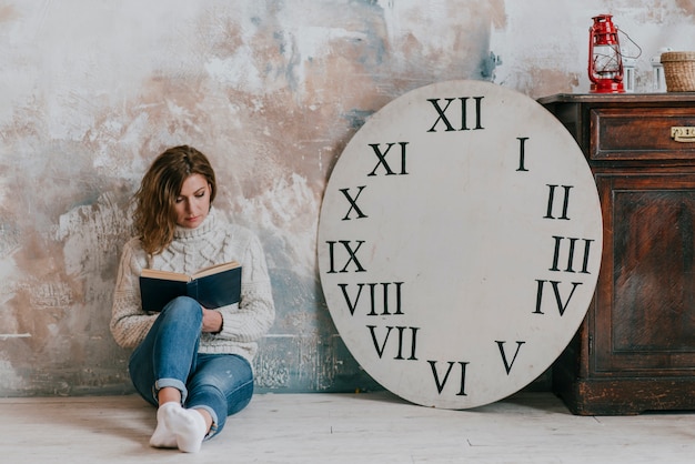 Woman reading book near clock disc