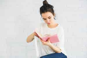 Free photo woman reading book near white wall