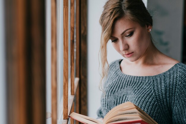 Woman reading book near window