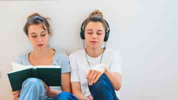 Free photo woman reading book sitting near the woman listening music on headphone