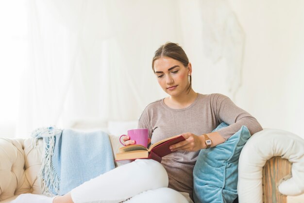 Woman reading book while holding coffee cup