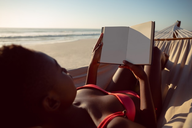 Woman reading a book while relaxing in hammock on the beach