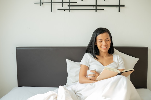 Woman reading book with cup of coffee at home in the bedroom.