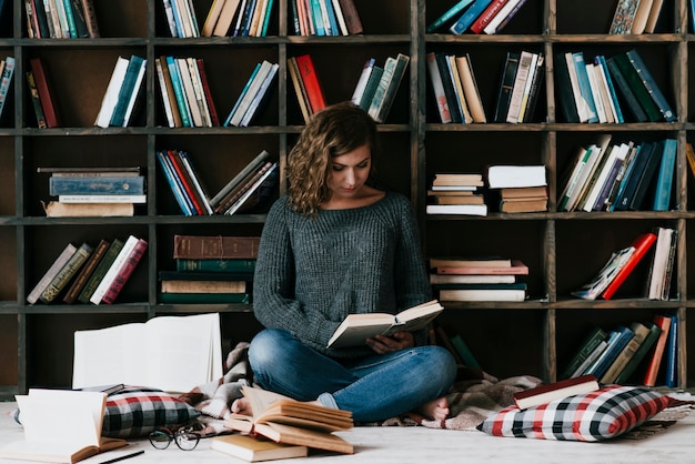 書棚の近くの床で読書する女性