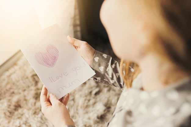 Woman reading greeting card with I love you mum inscription 