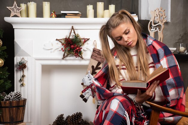 Woman reading interesting book near the fireplace. 