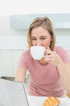 Женщина, читающая газету, имея кофе в кухне
