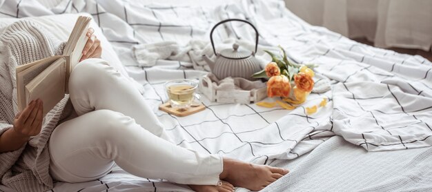 Woman reads a book in bed with tea and bouquet of tulips