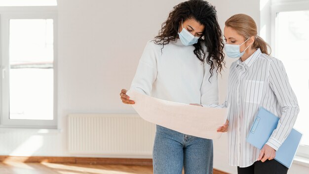 Woman and realtor looking at house plans together while wearing medical masks