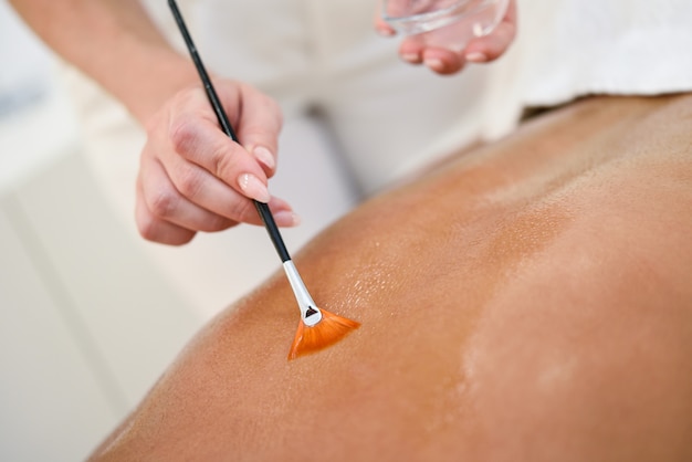 Woman receiving back massage treatment with oil brush