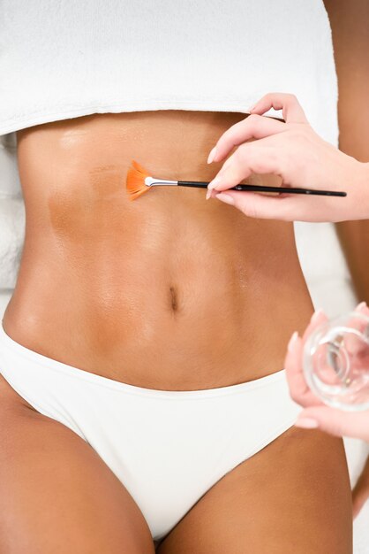 Woman receiving belly massage treatment with oil brush