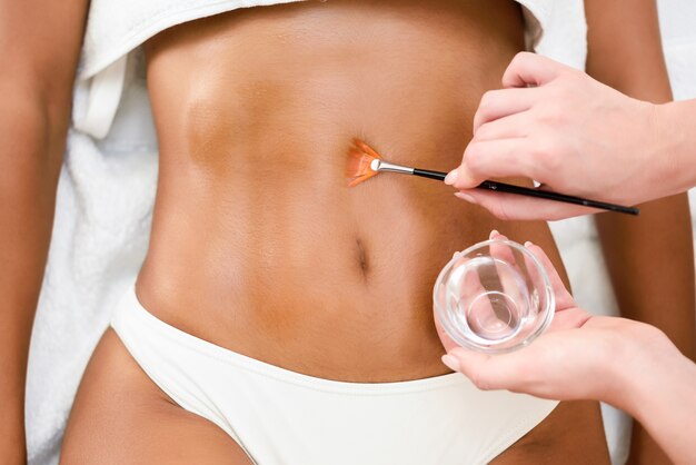 Woman receiving belly massage treatment with oil brush