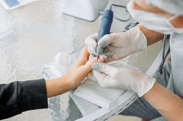 A woman receiving manicure from a woman in gloves and mask in beauty salon during daytime