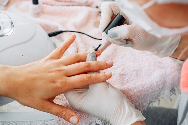 A woman receiving manicure from a woman in gloves and mask in beauty salon during daytime