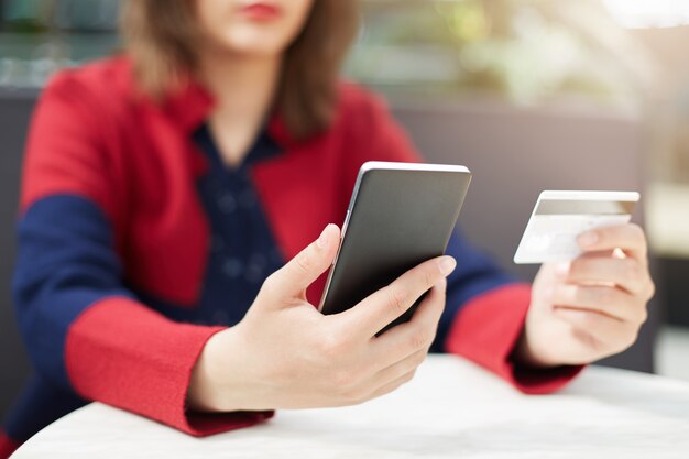 A woman in red clothes holding mobile phone in hands paying with credit card online