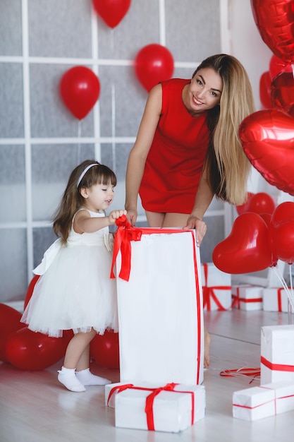 woman in red dress with little daughter open gift with balloons