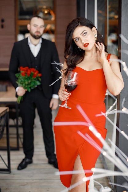 彼女のボーイフレンドを待っているレストランに立っている赤いエレガントなドレスの女性