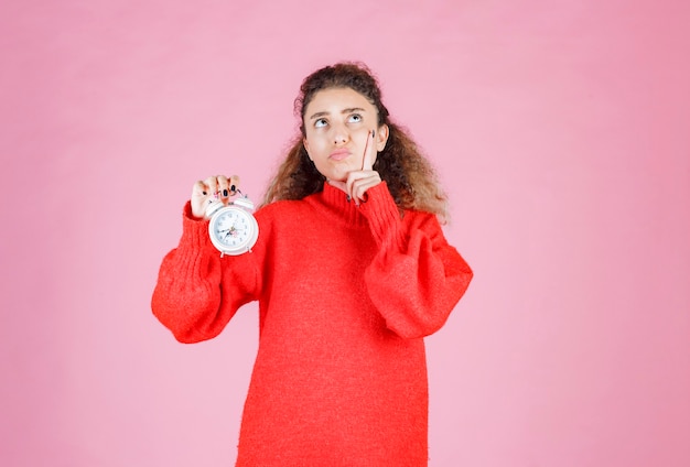 Free photo woman in red shirt holding alarm clock and thinking.