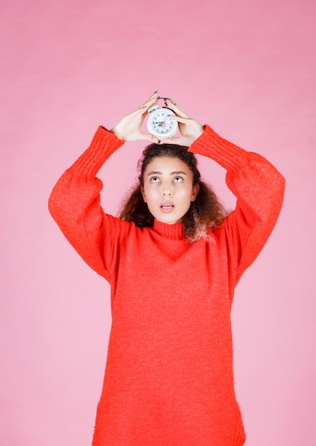 woman in red shirt holding alarm clock and thinking.