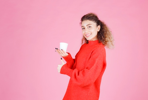 женщина в красной рубашке держит одноразовую кофейную чашку.