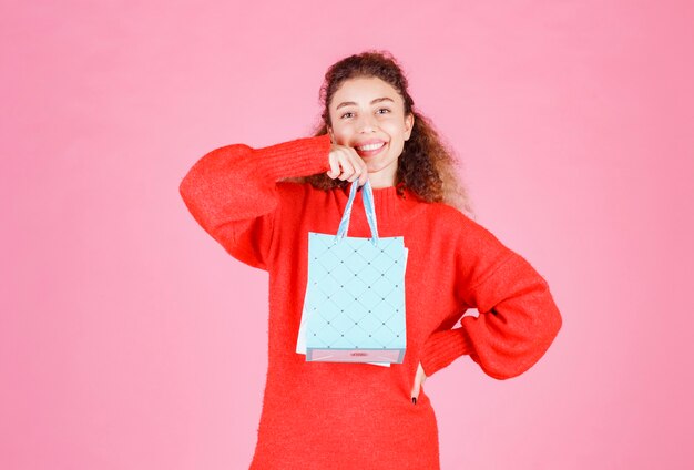 woman in red shirt holding multiple colorful shopping bags.