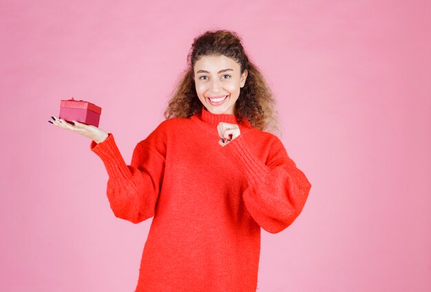 woman in red shirt holding a small red gift box.