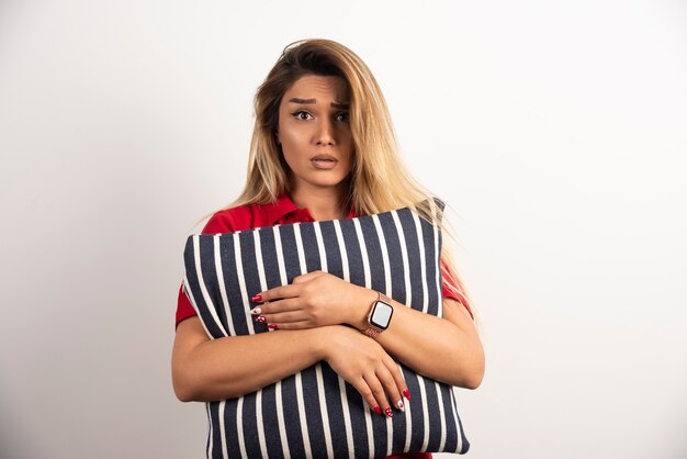 Woman in red shirt hugging a pillow on white background.