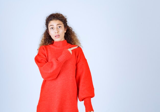 woman in red shirt pointing at somebody or somewhere with emotional face on blue. 