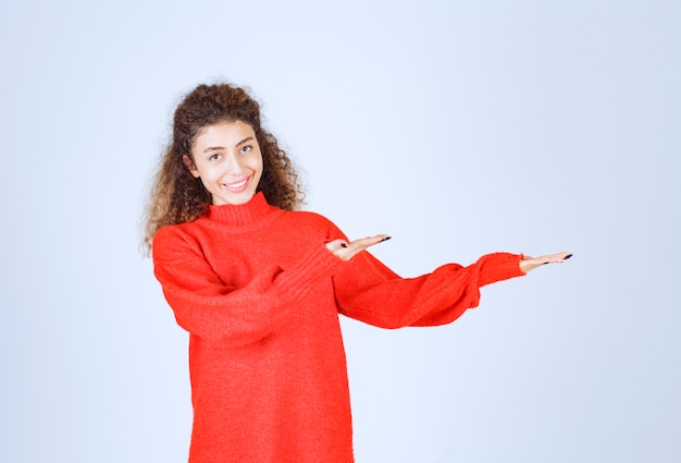 woman in red shirt pointing at somebody or somewhere with emotional face on blue. 