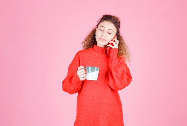 woman in red shirt talking to the phone while drinking coffee.