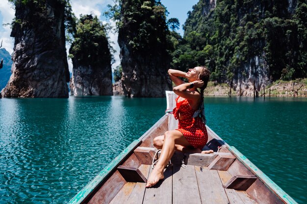 Woman in red summer dress on thai asian boat on vacation, travel around Thailand